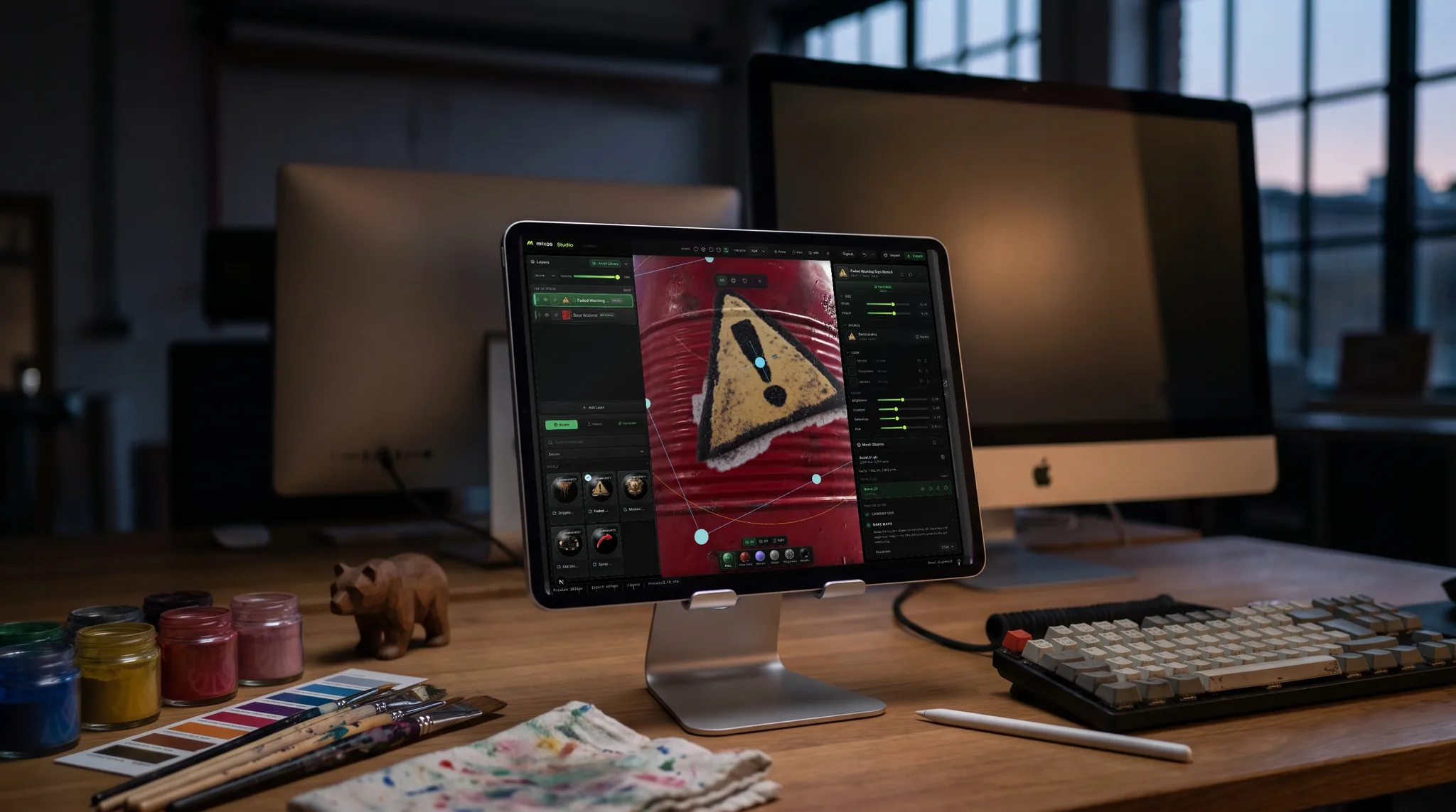 mixos Paint open on an iPad showing a red steel barrel with a weathered hazard decal being placed on it, on a desk at dusk, a second screen glowing softly out of focus behind it.